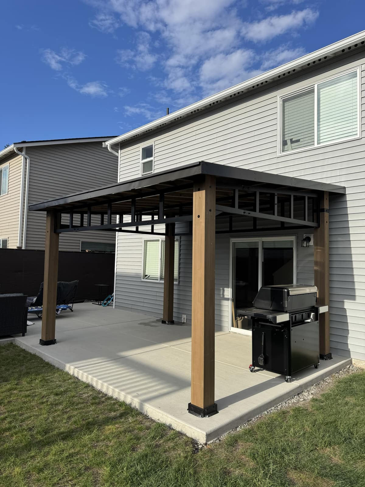 Cedar-post patio cover with dark metal roof attached to the home