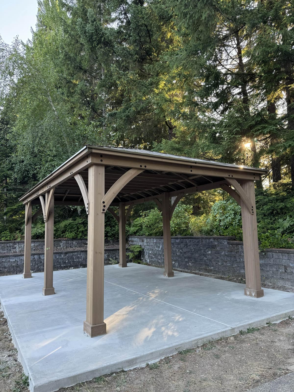 Cedar gazebo with metal roof on a concrete pad in a forest clearing at golden hour