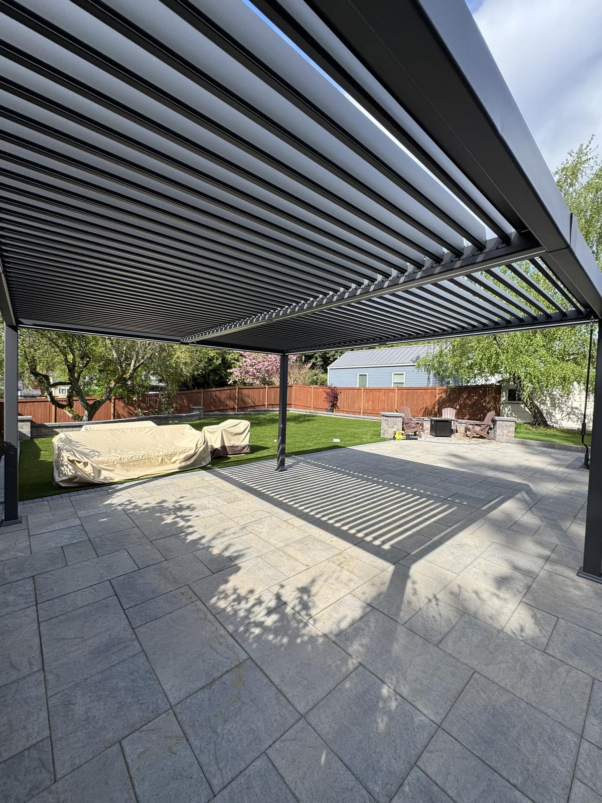 Dramatic underside view of a black louvered pergola over a large paver patio