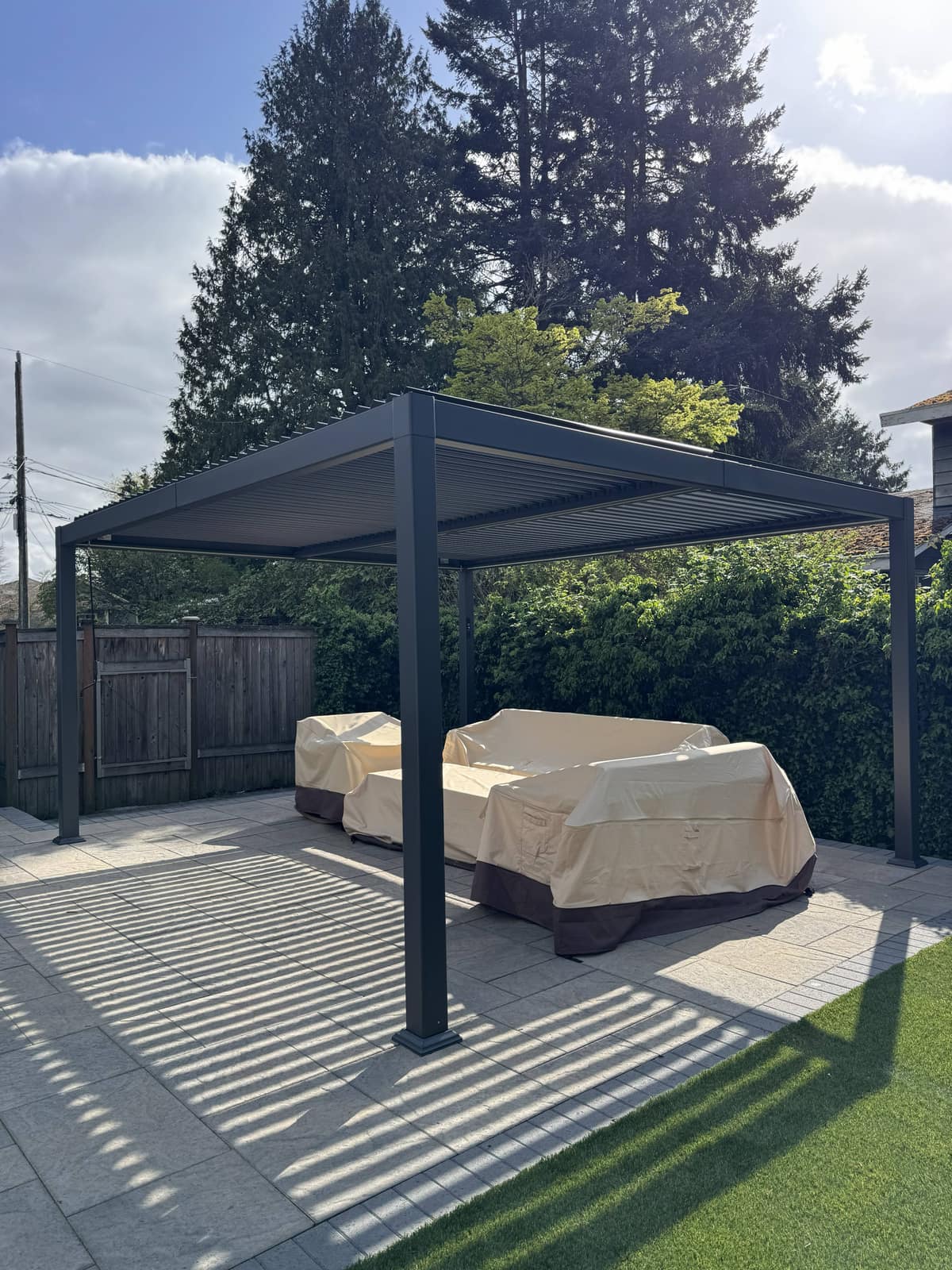 Black louvered pergola on a gray paver patio with lounge seating in full sun