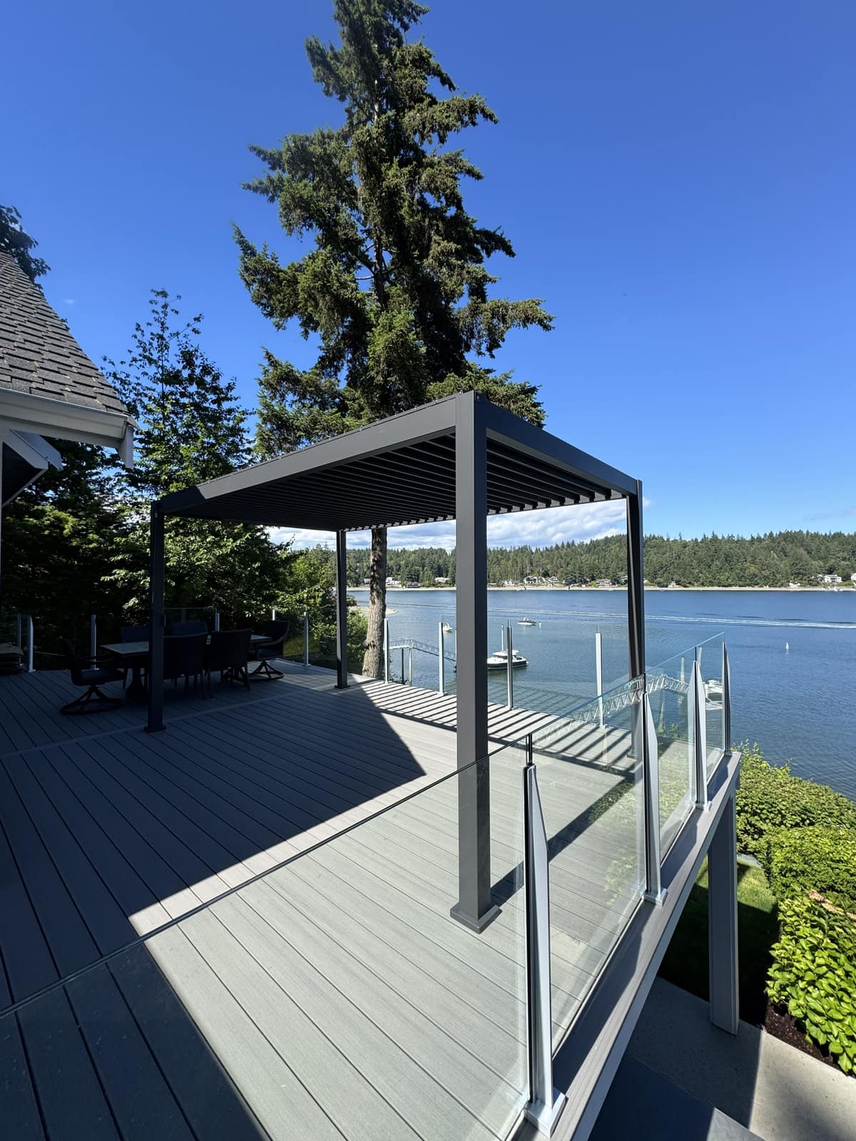 Black louvered aluminum pergola on a waterfront deck overlooking the bay